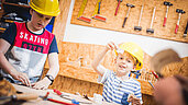 Drei Kinder mit Bauarbeiterhelmen basteln in der Kinderwerkstatt des Familienhotels Landgut Furtherwirt.