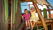 Zwei Kinder mit bunt bemalten Gesichtern spielen auf dem Outdoor-Spielplatz im Familienhotel Spa- & Familien-Resort Krone im Allgäu.