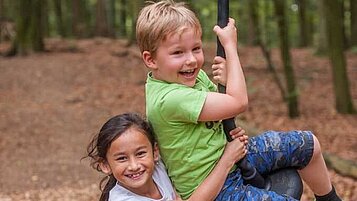 Zwei Kinder spielen im Waldkinderclub des Familienhotels Landhaus zur Ohe im Bayerischen Wald an einer Tellerschaukel.