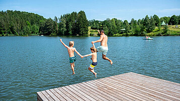Drei Jungs springen vom Steg in den Eginger See im Bayerische Wald.