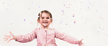 Ein Mädchen freut sich über viele Luftballons und Konfetti.