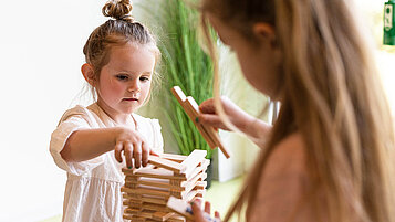Mädchen baut in der Kinderbetreuung im Familienhotel mit Holzklötzen einen Turm.