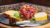 Verschiedene Käsesorten und Weintrauben angerichtet auf einer Platte am Buffet des Familienhotels Landhuus Laurenz.