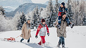 Winter im Salzburger Land: Familie wandert im Schnee mit einem Schlitten. Sohn sitzt auf Papas Schultern.
