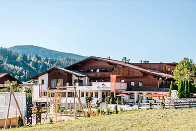 Das Familienhotel Das Hopfgarten in Tirol bei strahlenden Sonnenschein von außen. Auf dem Hotelgelände befindet sich ein großzügiger Outdoor-Spielplatz.