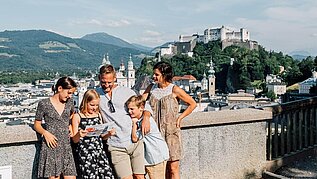 Familie steht in der Salzburger Altstadt, im Hintergrund zu sehen ist die Festung.