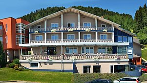 Außenansicht des Hotels Alpengasthof Hochegger im Sommer. Die Balkone vor der hellen Fassade sind mit schönen Blumenkästen dekoriert.
