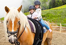 Zwei Kinder reiten auf einem Pony im Familienhotel Familien Resort Petschnighof in Kärnten.
