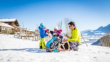 Eltern sitzen mit ihren beiden Kindern auf einem Schlitten im Schnee.