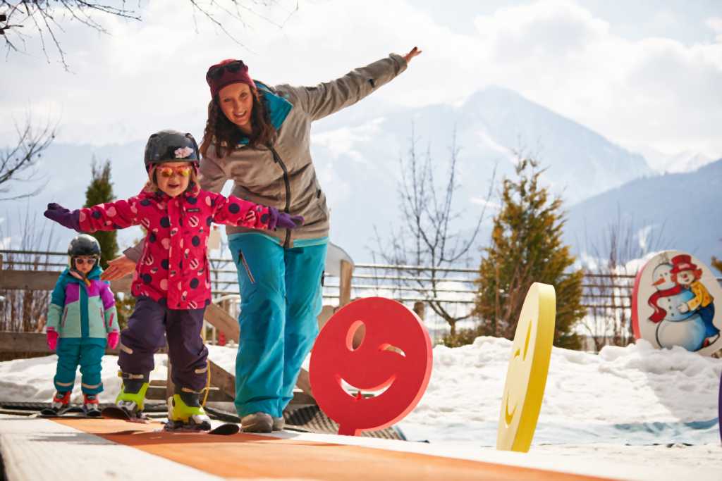 Skilehrerin bringt zwei kleinen Mädchen auf dem Zauberteppich des Familienhotels Amiamo das Skifahren bei.