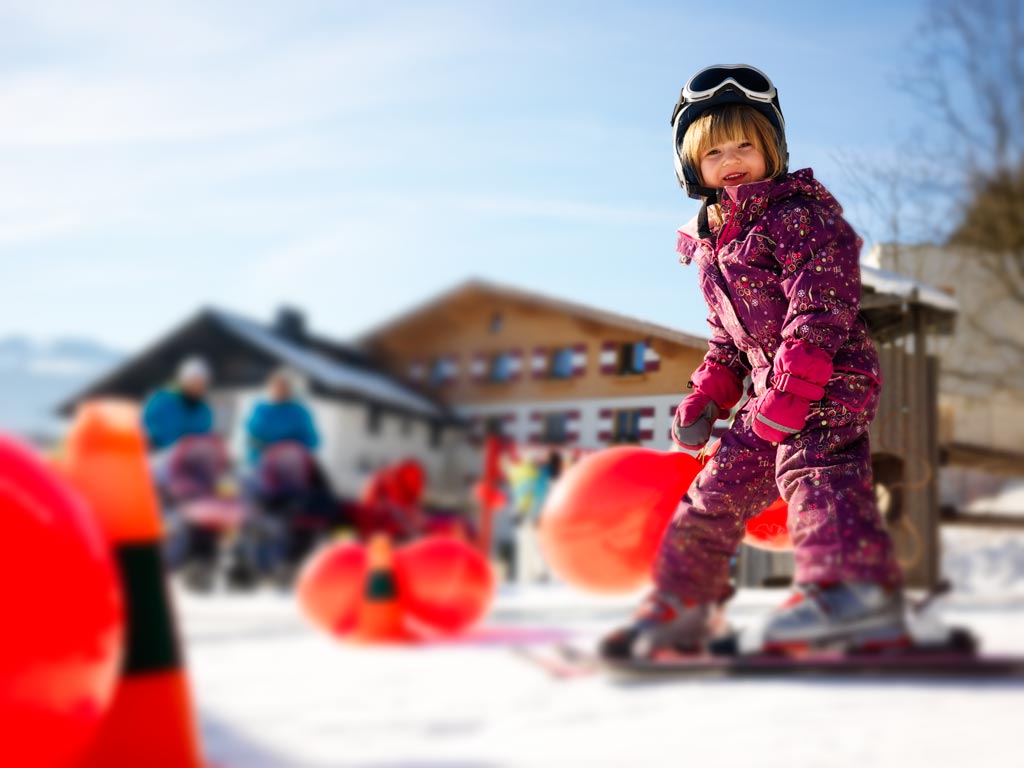 Skilehrerin bringt zwei kleinen Mädchen auf dem Zauberteppich des Familienhotels Amiamo das Skifahren bei.