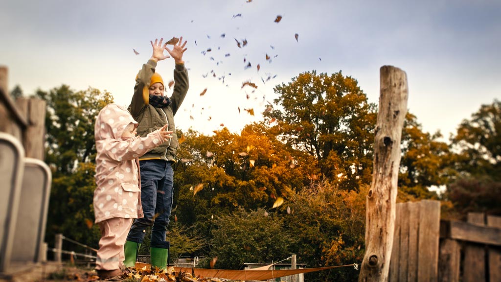 Zwei Kinder spielen mit dem Laub auf dem Außenspielplatz des Familienhotels Landhaus Averbeck in der Lüneburger Heide.