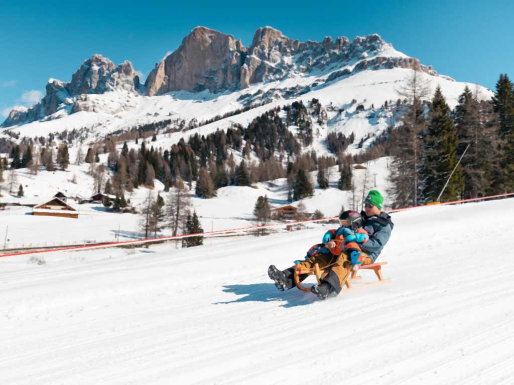 Vater und Sohn rodeln in Südtirol die Piste runter, bevor es wieder ins Familienhotel Engel Gourmet & Spa geht.