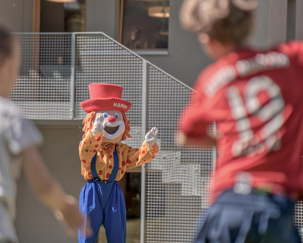 Maskottchen Happy spielt mit den Kindern in der Kinderbetreuung des Familienhotels Gorfion Fußball