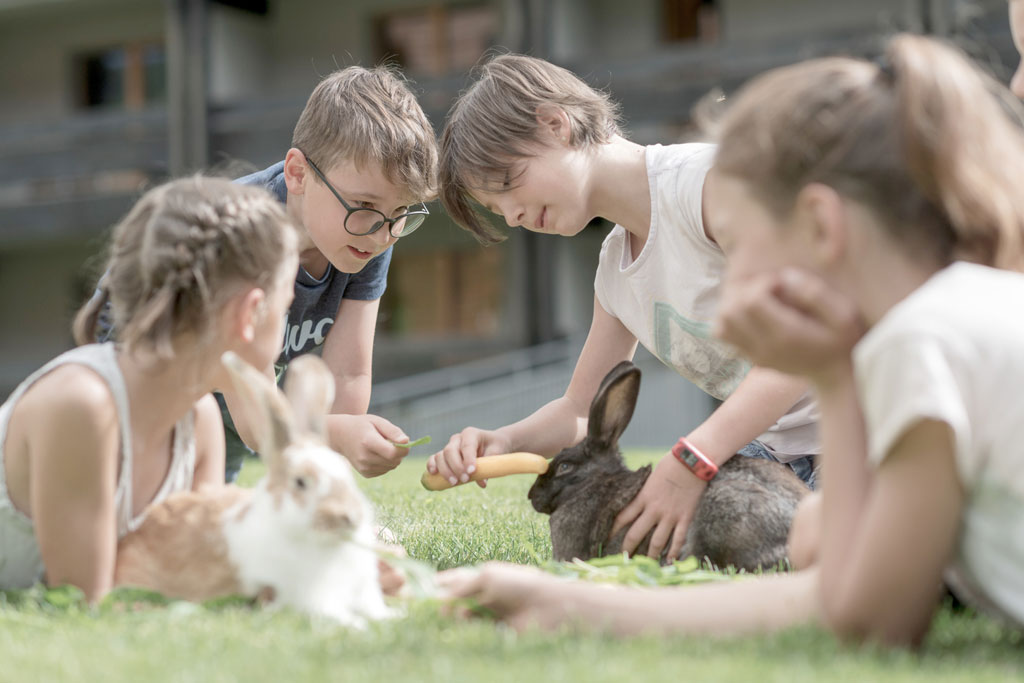 Kinder liegen auf der Wiese und streicheln die Hasen im Familienhotel Gorfion in Lichtenstein.