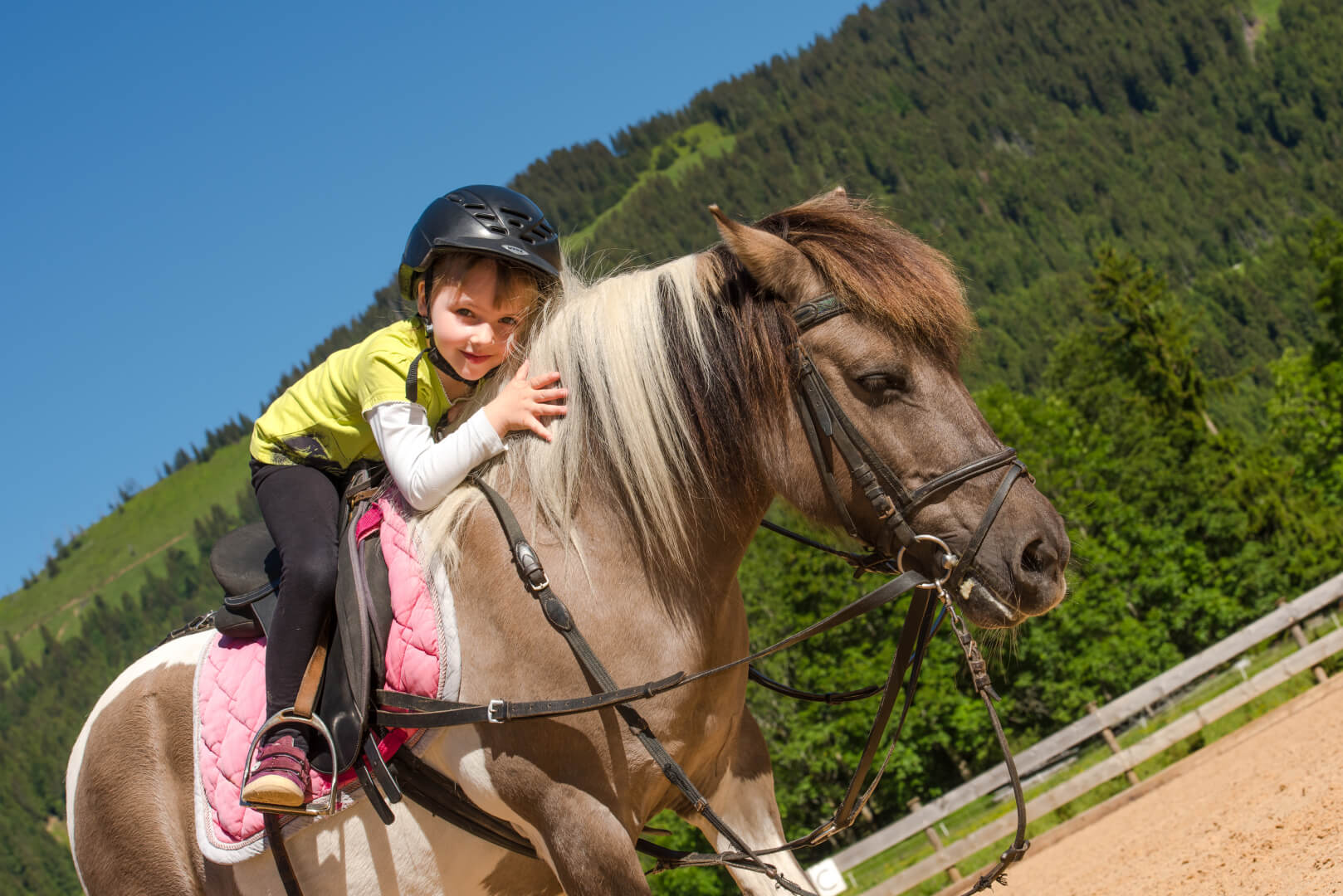 Mädchen sitzt auf dem Reitplatz des Spa- & Familien-Resorts Krone einem Pferd und kuschelt das Tier. 