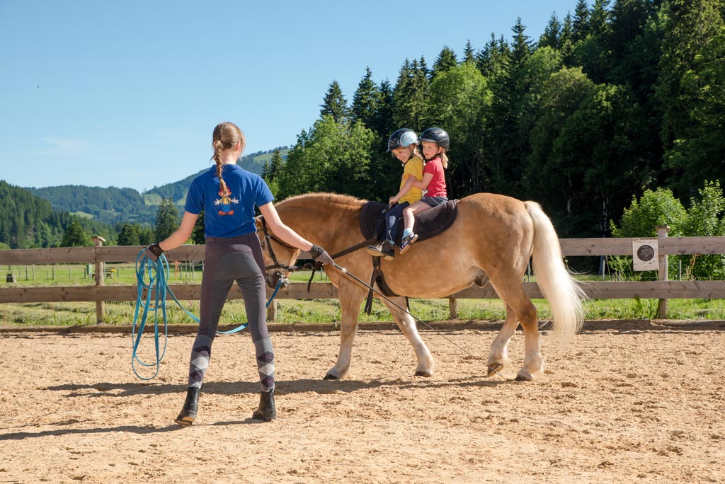 Mädchen sitzt auf dem Reitplatz des Spa- & Familien-Resorts Krone einem Pferd und kuschelt das Tier. 