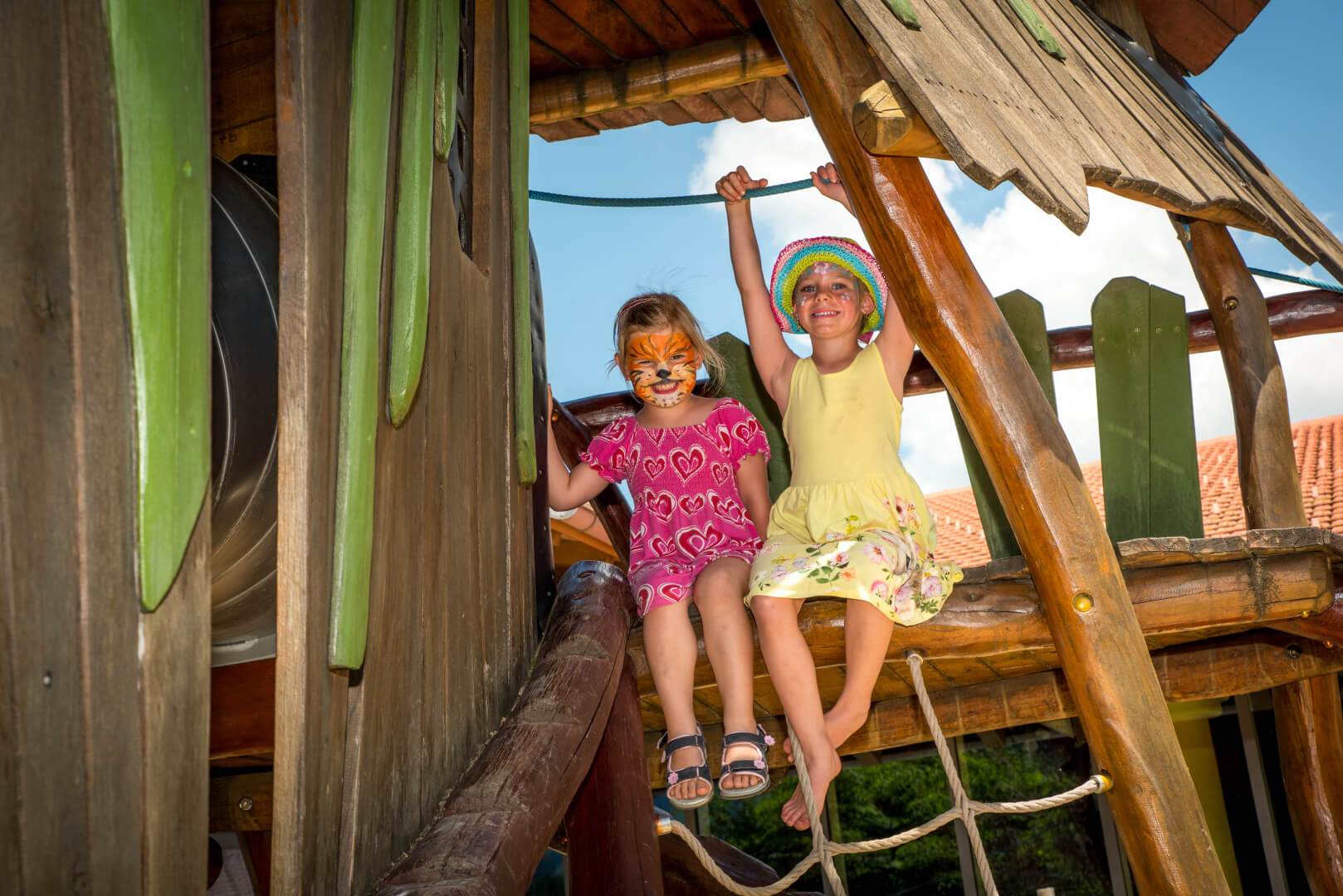 Zwei Kinder mit bunt bemalten Gesichtern spielen auf dem Outdoor-Spielplatz im Familienhotel Spa- & Familien-Resort Krone im Allgäu.