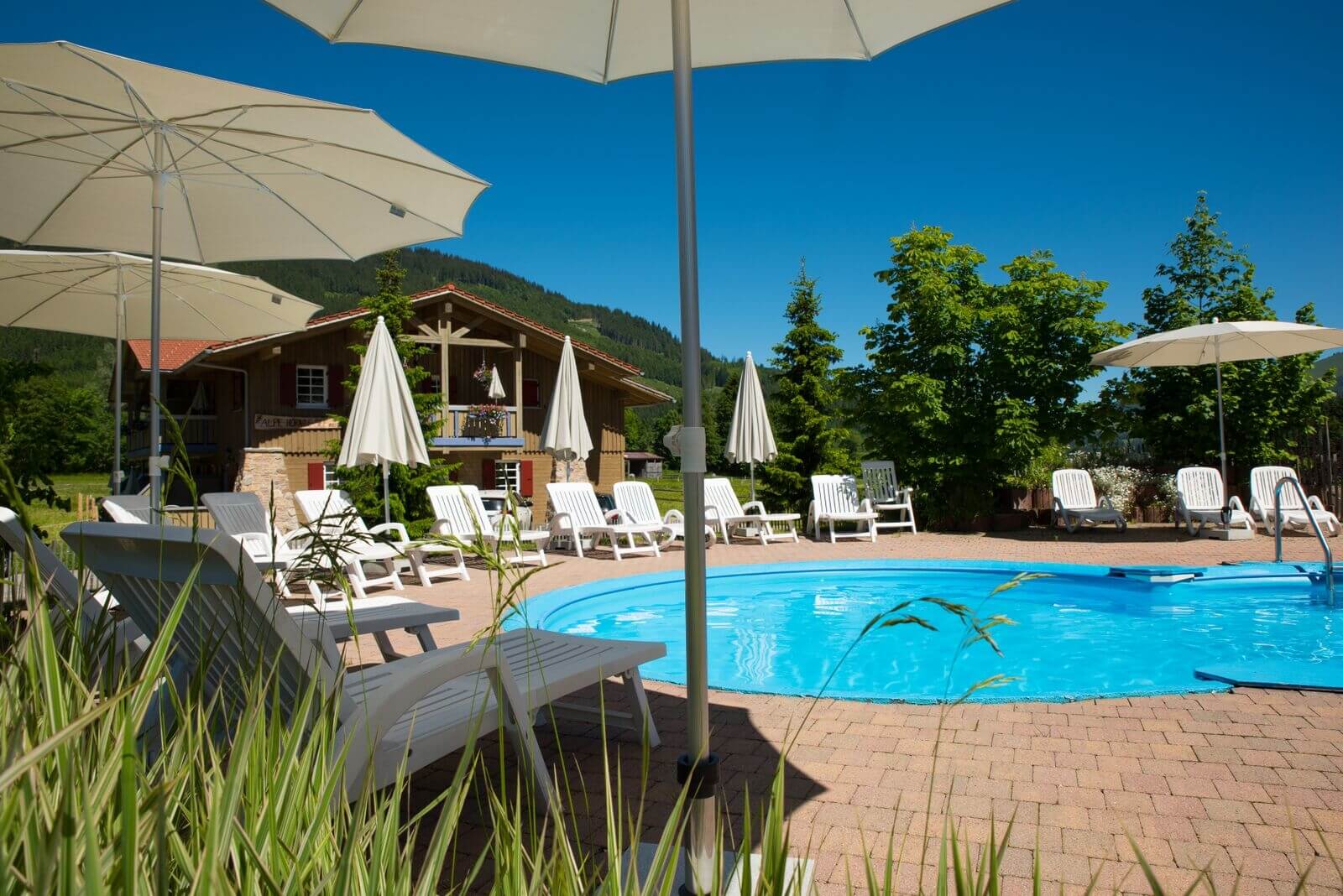 Ein Pool imt Liegemöglichkeiten und Blick auf die Berge im Familienhotel Spa- & Familien-Resort Krone in den Allgäuer Alpen.