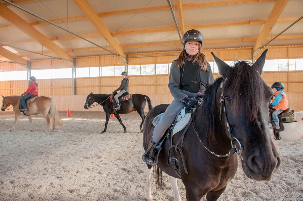 Mädchen sitzt auf einem Pferd und reitet in der Reithalle des Familienhotels Landhaus zur Ohe.