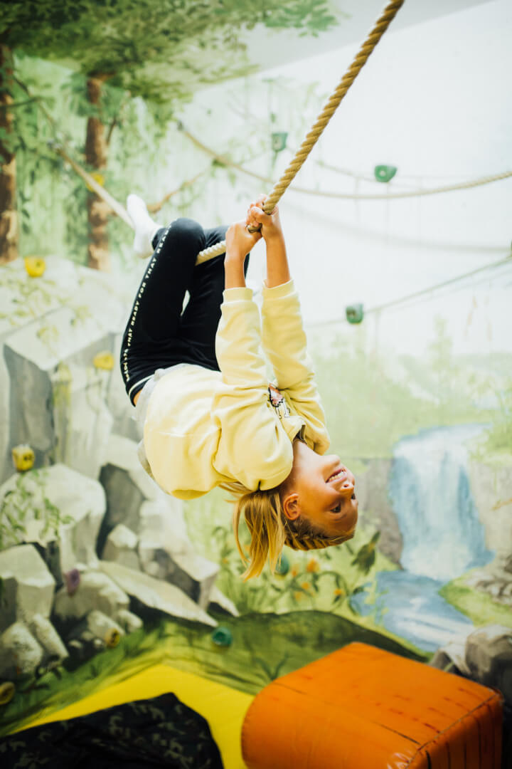 Mädchen klettert kopfüber an einem Seil im Happy-Club des Kinderhotels Sailer in Tirol.