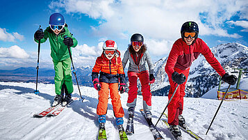 Eine Familie freut sich schon aufs Skifahren im Winter im Allgäu. Der Tag ist sonnig und der Himmel blau.