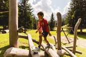 Ein Junge geht über ein großes Holzspielzeuggerüst auf dem Outdoorspielplatz am Almfamilyhotel Scherer in Tirol 
