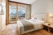 Helles Zimmer im Hotel Bella Vista in Südtirol mit Doppelbett, Holzfußboden und Balkon mit Bergblick.