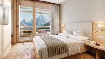 Helles Zimmer im Hotel Bella Vista in Südtirol mit Doppelbett, Holzfußboden und Balkon mit Bergblick.