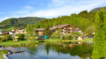 Außenansicht des Familienhotels Landgut Furtherwirt im Sommer mit einem Naturbadeteich direkt vor der Tür.