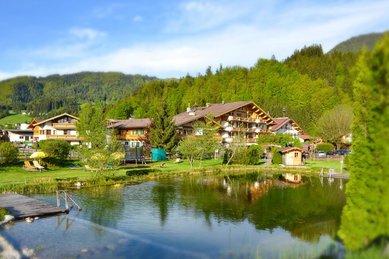 Außenansicht des Familienhotels Landgut Furtherwirt im Sommer mit einem Naturbadeteich direkt vor der Tür.