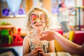 Fröhliches Mädchen mit Schmetterlings-Gesichtsfarbe genießt eine kreative Kinderbetreuung im Landgut Furtherwirt