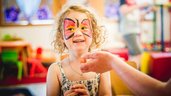 Fröhliches Mädchen mit Schmetterlings-Gesichtsfarbe genießt eine kreative Kinderbetreuung im Landgut Furtherwirt