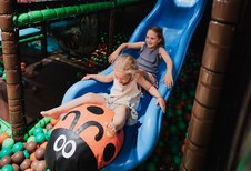 Zwei Kinder rutschen gemeinsam auf einer blauen Rutsche mit Marienkäfer-Motiv in der Indoor-Spielwelt des Familienhotels Tirolerhof.