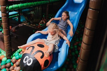 Zwei Kinder rutschen gemeinsam auf einer blauen Rutsche mit Marienkäfer-Motiv in der Indoor-Spielwelt des Familienhotels Tirolerhof.