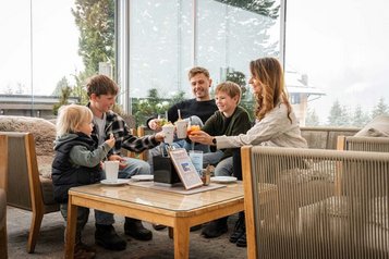 Familie stößt auf der gemütlichen Terrasse des Familienhotels Alpengasthof Hochegger mit Getränken an
