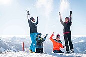Eine Familie spielt im Schnee und wirft ihn um sich im Familienurlaub im Familienhotel Das Hopfgarten in Tirol.