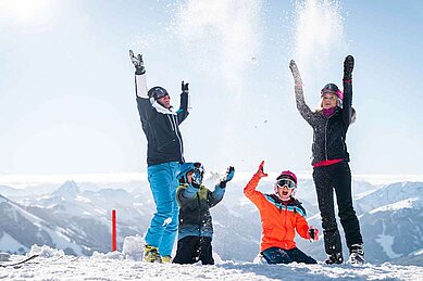 Eine Familie spielt im Schnee und wirft ihn um sich im Familienurlaub im Familienhotel Das Hopfgarten in Tirol.
