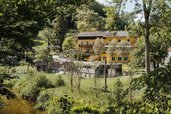 Das Kinderhotel Bruckwirt in Oberösterreich ist aus erhöhter Perspektive mit Fluss im Vordergrund zu sehen.