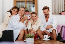 Familie entspannt in Bademänteln bei Kaffee und Getränken in der Outdoor-Lounge des Familienhotels Amiamo.