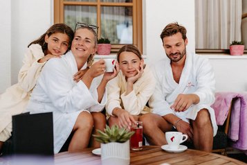 Familie entspannt in Bademänteln bei Kaffee und Getränken in der Outdoor-Lounge des Familienhotels Amiamo.