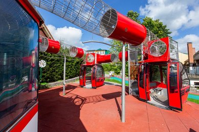 Abenteuerlicher Außenspielplatz mit roten Gondel-Spielgeräten, Röhren und Kletterelementen im Hotel Engel im Schwarzwald