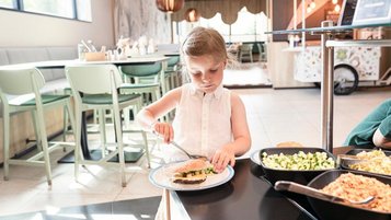 Ein Mädchen belegt ihren Burger am Salatbuffet im Familotel ganz nach ihrem Geschmack.