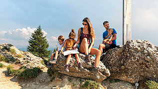 Familie pausiert am Gipfelkreuz von der schönen Familienwanderung in Vorarlberg.