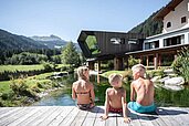 Am hauseigenen Badesee mit Steg sitzen Kinder in der Sonne. Freut euch auf perfekte Urlaubsmomente im Familienurlaub im Alphotel Tyrol in Südtirol.
