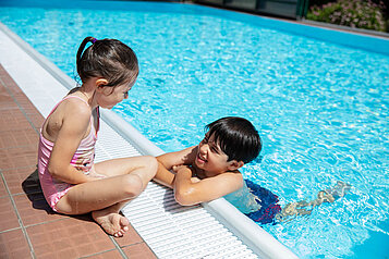 Zwei Kinder am Pool reden miteinander im Familienhotel Bruckwirt in Oberösterreich.