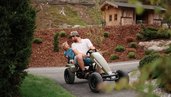 Vater fährt mit seinem Sohn im Gokart durch die Gartenanlage im Familienhotel Habachklause Salzburger Land.