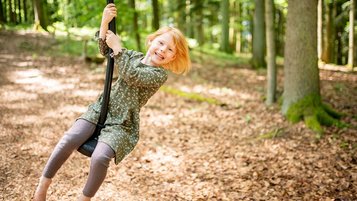Ein fröhliches Mädchen schwingt lachend an einem Seilspielgerät im Waldspielplatz des Familienhotels Landhaus zur Ohe