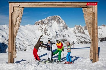 Eine Familie posiert fröhlich auf Skiern vor einem Holzrahmen mit Bergpanorama im Skigebiet nahe dem Familienhotel Ramsi in Kärnten
