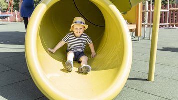 Ein Kind rutscht auf dem Spielplatz des Familienhotel Kaiserhof in Tirol durch eine gelbe Röhrenrutsche.